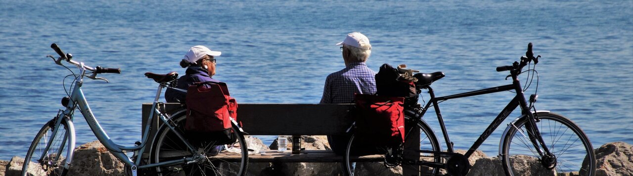 Zwei ältere Menschen sitzen auf einer Bank mit Aussicht auf den See