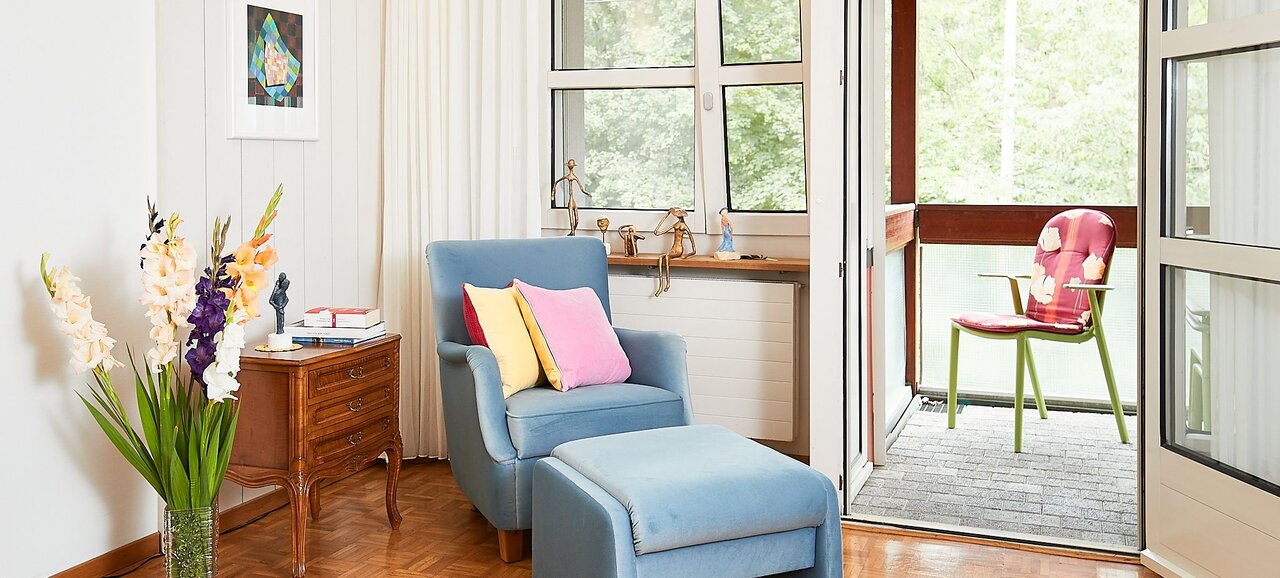 Ein Ausschnitt eines Bewohnerzimmers mit geschmackvoller Möblierung, Bildern an der Wand und Büchern auf dem Regal. Mit im Bild der Balkon, über den die meisten Zimmer in der Mühlehalde verfügen.